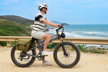 Man riding the gray Burchda R5 Pro fat tire e-bike along a coastal dirt road, utilizing its 20Ah large battery for a long-range trip.